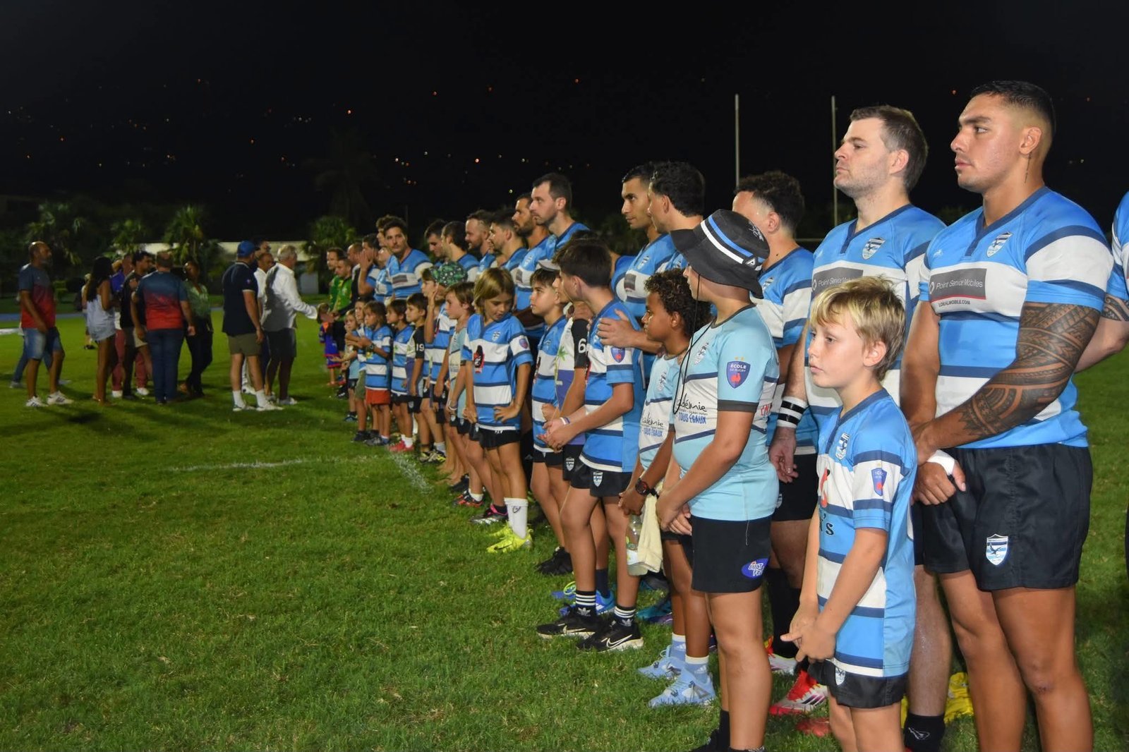 Les seniors et les enfants du club alignés côte à côte avant le coup d'envoi au Stade Delgard